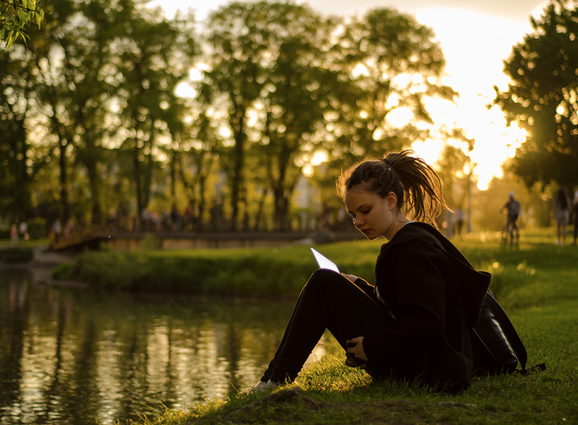 Young woman sitting next to the pond while looking at her phone